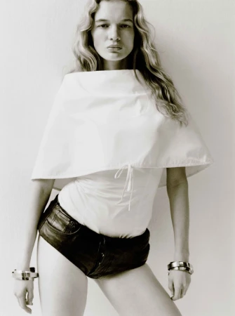 Monochrome portrait of a female model in a white top and dark shorts, accented with bracelets, posing against a neutral backdrop.