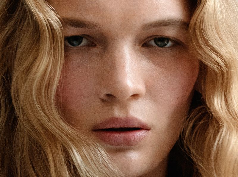 Close-up portrait of a fair-skinned, light-haired young adult woman looking directly at the camera, with a neutral facial expression.