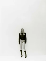 Model standing against a plain white background wearing a dark jacket, light shorts, knee socks, and flat shoes.