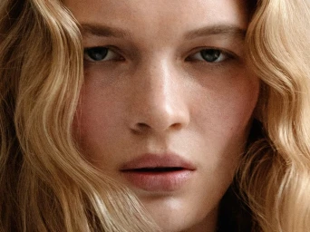 Close-up portrait of a woman with blonde wavy hair and freckles looking directly into the camera.