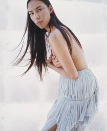 Model Quannah ChasingHorse with long dark hair wearing a light grey pleated skirt against a white seamless backdrop