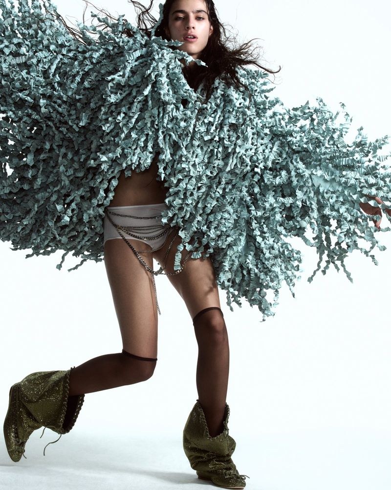 Fashion shot of a woman in a fuzzy jacket, shorts, and boots, striking a pose in a studio setting with a clean white background.
