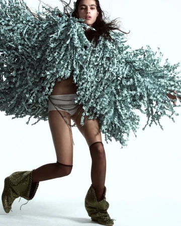 Fashion shot of a woman in a fuzzy jacket, shorts, and boots, striking a pose in a studio setting with a clean white background.