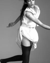 Model Loli Bahia in a white blouse and skirt with black stockings against a grey backdrop for Pop Magazine