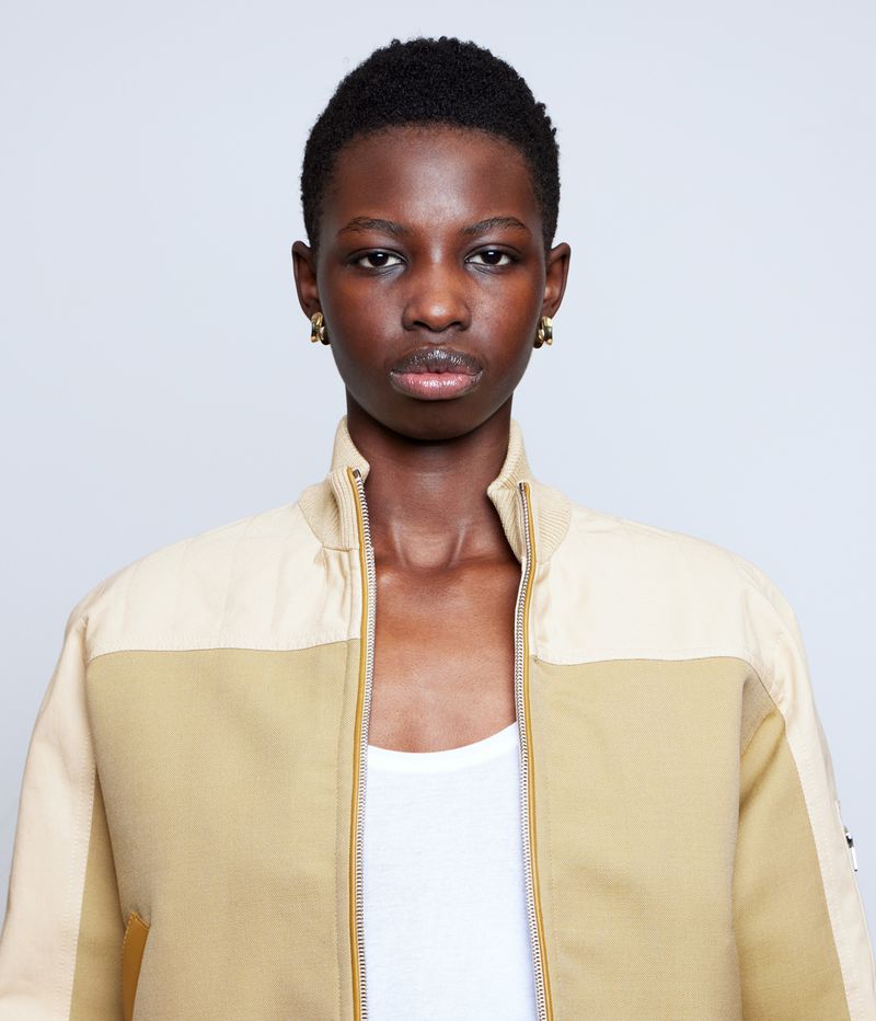 Close-up studio shot of a stylish African woman in a two-tone bomber jacket, accessorized with gold earrings, against a plain white backdrop.