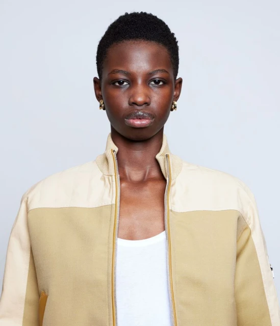 Close-up studio shot of a stylish African woman in a two-tone bomber jacket, accessorized with gold earrings, against a plain white backdrop.