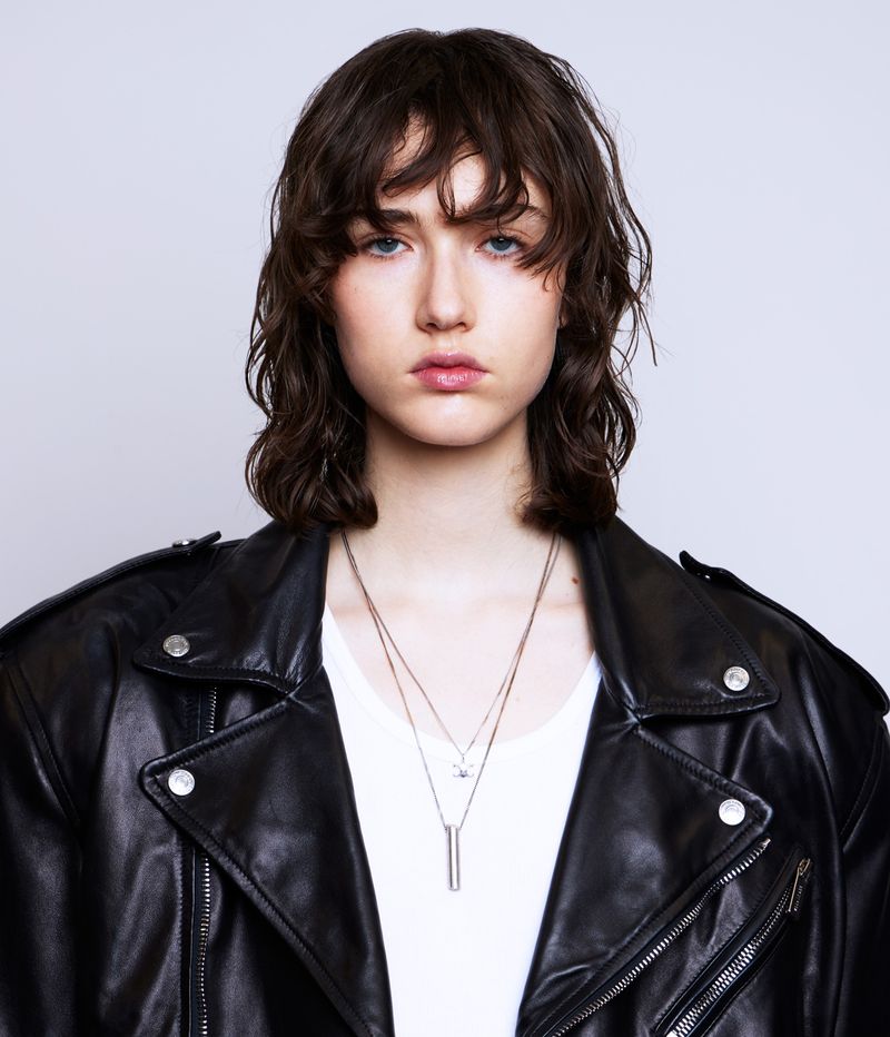 Portrait of a model wearing a black leather jacket and necklaces against a white studio background.