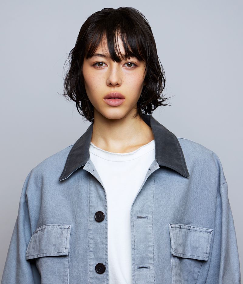 Portrait of a model wearing a blue jacket with a dark collar over a white t-shirt against a grey studio backdrop.