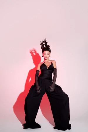 Model in avant-garde black structured outfit and intricate sculptural updo with dramatic red cast shadow on white backdrop