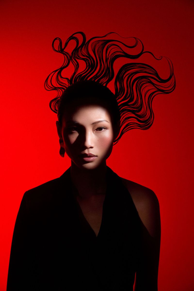 Dramatic portrait of a person with an Asian appearance in black clothing against a bold red backdrop, using shadows for emphasis.