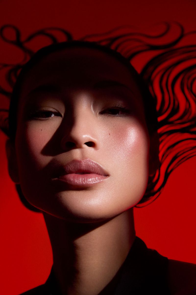 Close-up portrait of an East Asian woman with dramatic shadow cast across her face against a bold red background.