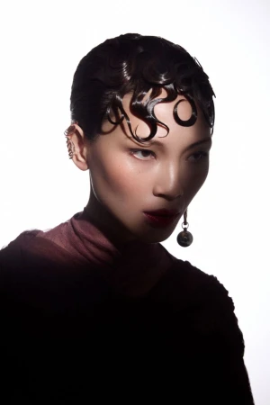 Close-up portrait of an East Asian model with slicked wet hair styled in finger waves wearing dark clothing and drop earrings.