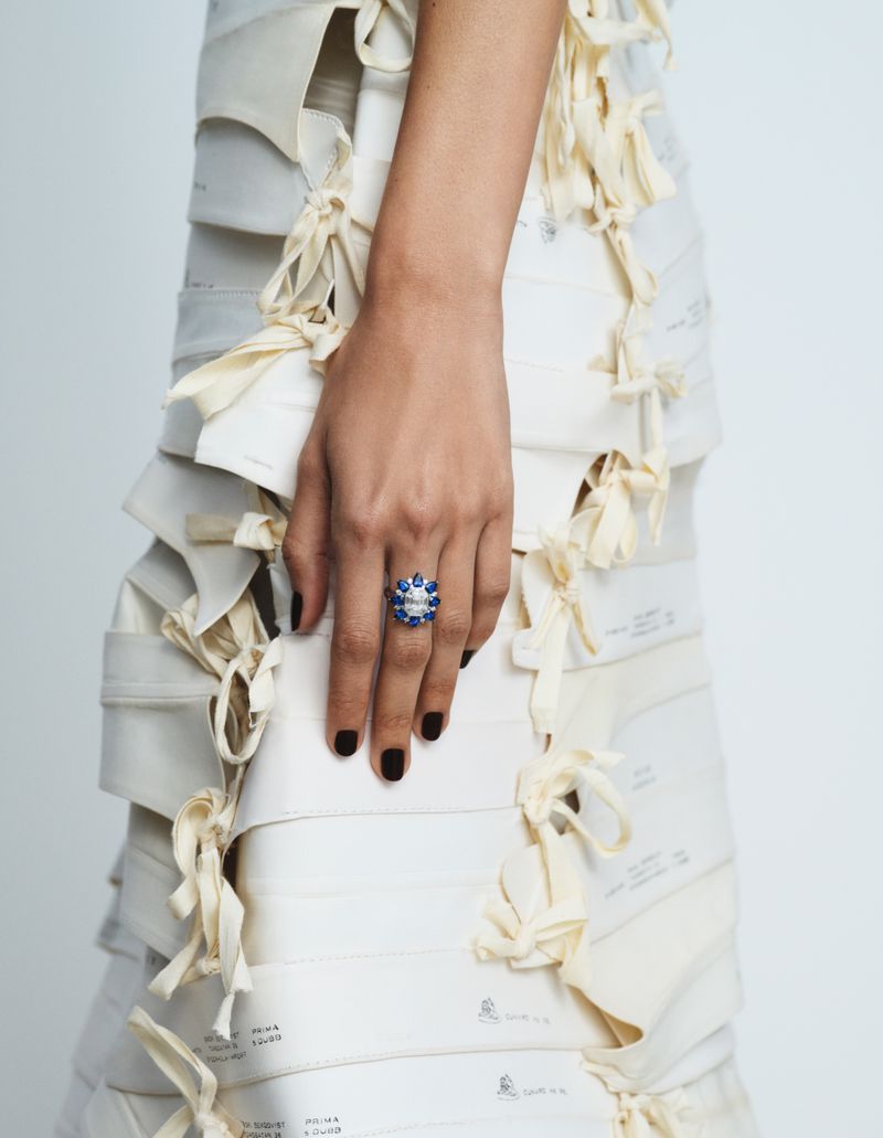 Close-up shot of a fair-skinned person wearing a large blue and white gem ring and a dress made of pattern paper with cream ties.