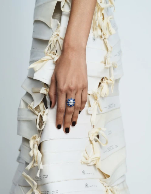 Close-up shot of a fair-skinned person wearing a large blue and white gem ring and a dress made of pattern paper with cream ties.