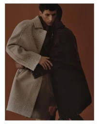 Two male models embracing closely against a warm brown background in a fashion editorial shot.