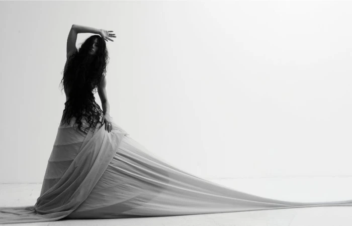 Model with long dark hair wearing a voluminous trailing gown in a studio setting.