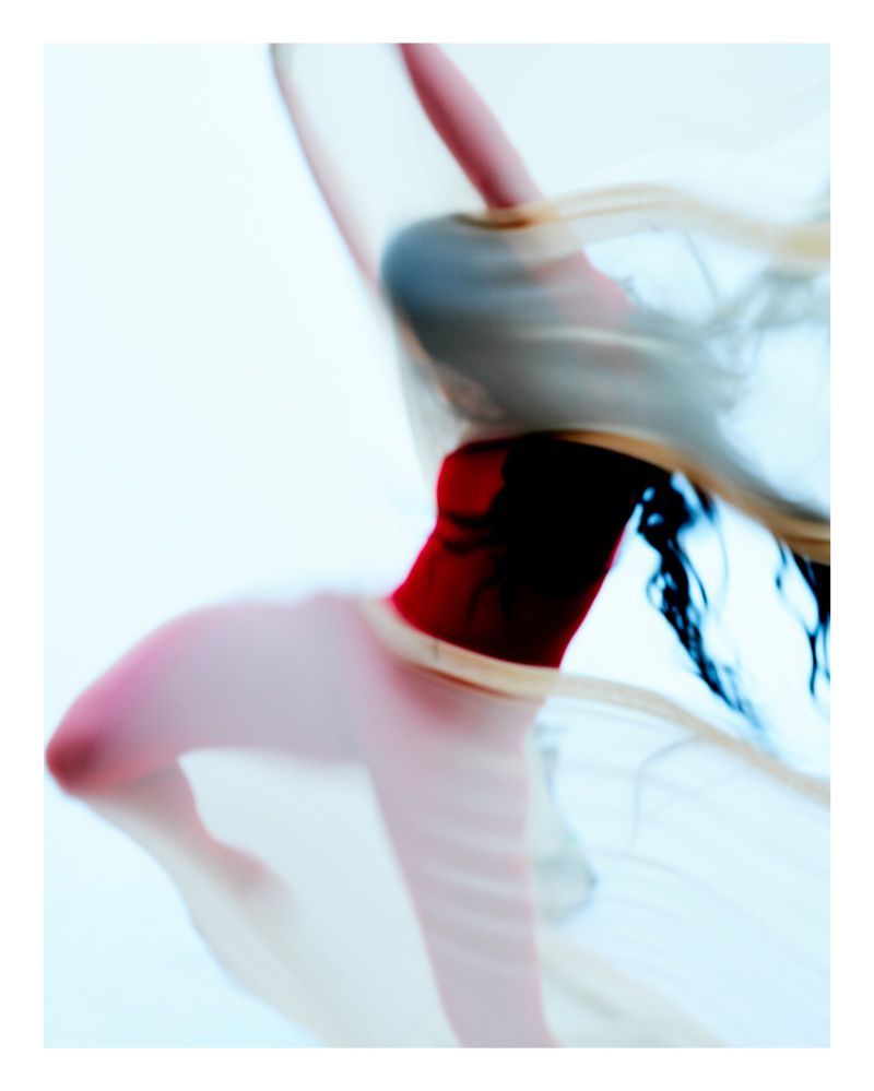 Blurred image of a dancer with a translucent fabric and a red leotard against a white background, creating a sense of movement and grace.
