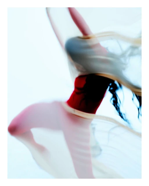 Blurred image of a dancer with a translucent fabric and a red leotard against a white background, creating a sense of movement and grace.