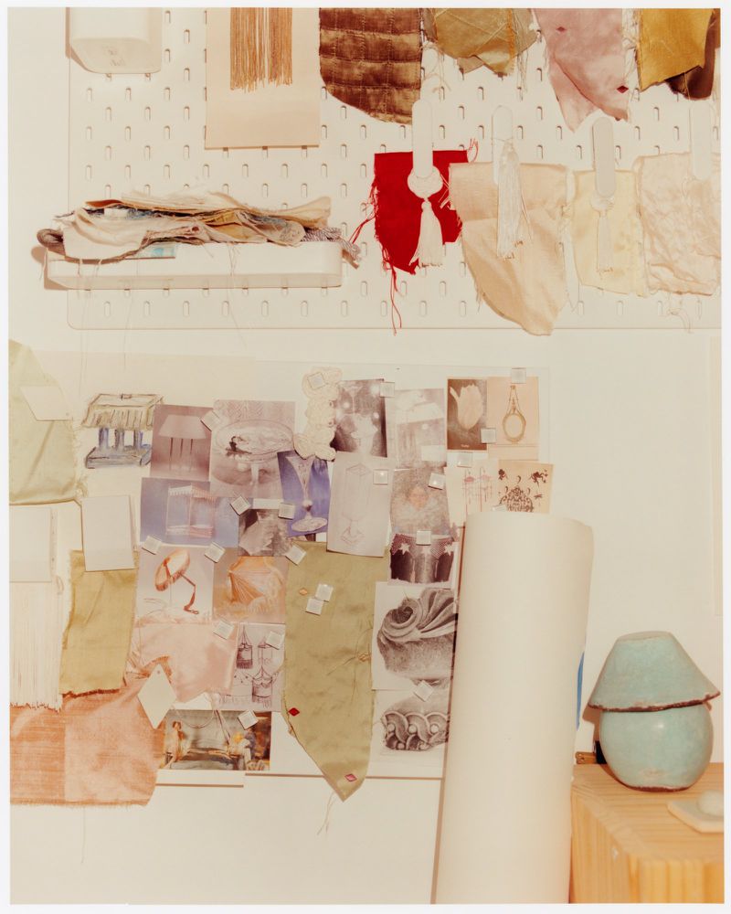 Display board with textile swatches, material samples, and photos attached to a white pegboard, casting soft, diffused light on the presentation.