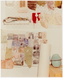 Studio mood board covered in fabric swatches and reference photos with a small blue ceramic lamp on a wooden desk