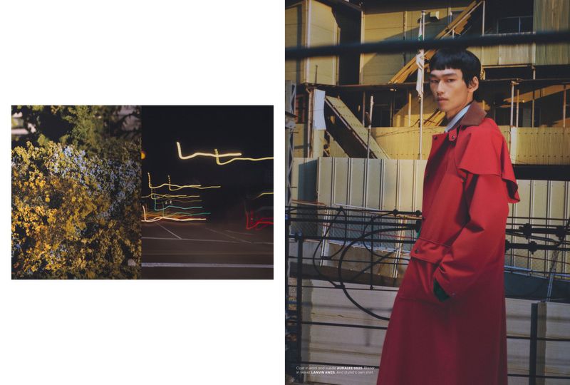 Fashion shot of an Asian adult male model in a red trench coat standing in an outdoor urban setting with an industrial background.