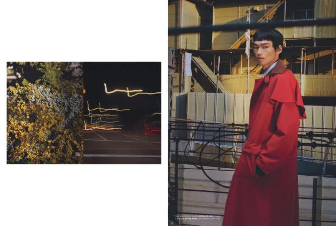 Model wearing a bright red trench coat standing on a rooftop balcony with industrial buildings in the background.