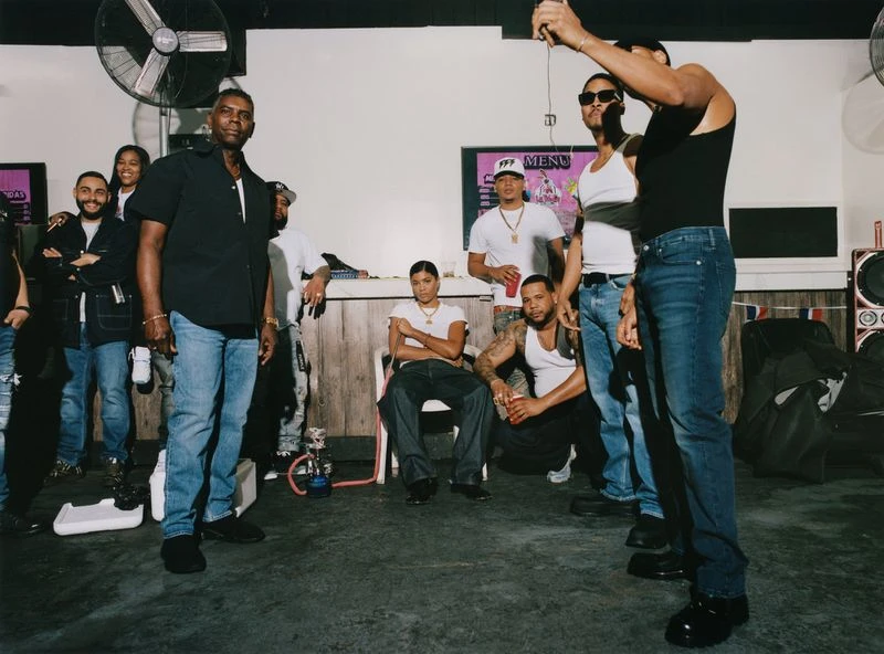 Indoor shot of a diverse group of people, men and women, standing and sitting, in casual clothing in a room with basic furnishings.
