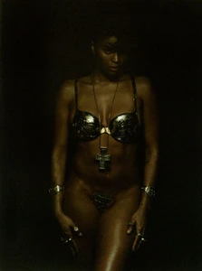 Woman wearing a metallic bra and cross pendant against a dark, low-key background