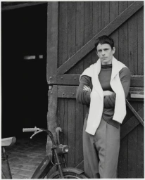 A man standing with arms crossed against a wooden barn door next to a moped for Les Echos Weekend.