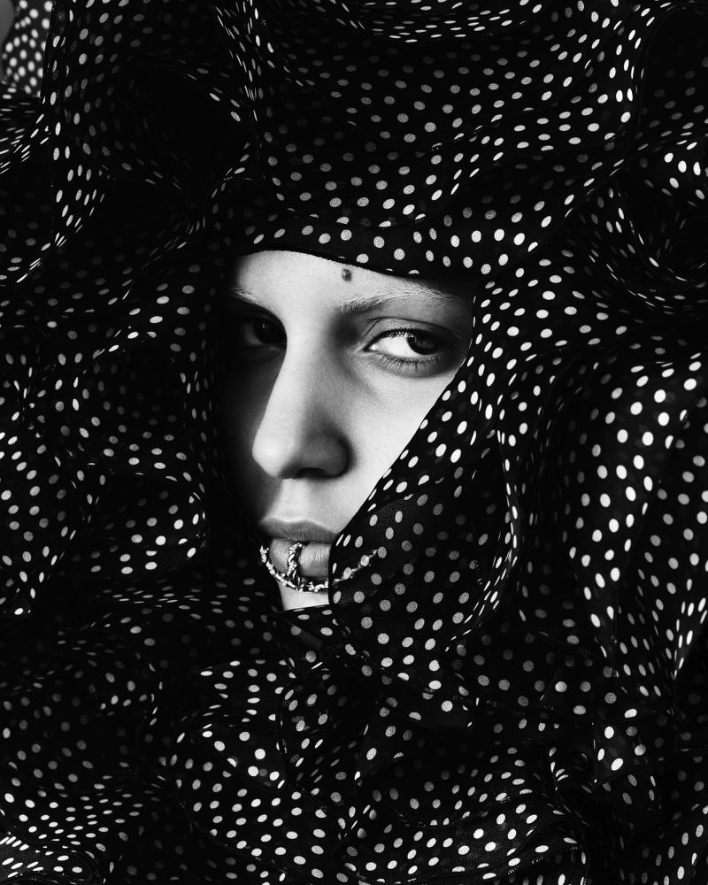 Black and white portrait of a woman surrounded by a polka dot textile, highlighting her face, lips, and silver lip ring.