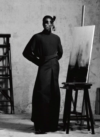 Fashion shot in grayscale featuring an African woman wearing black clothing, standing next to a black painting easel and ladder.