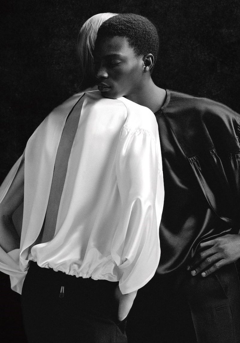 Black and white portrait of two fashion models in flowing blouses, one Black man in black top, one light-skinned person in white top.