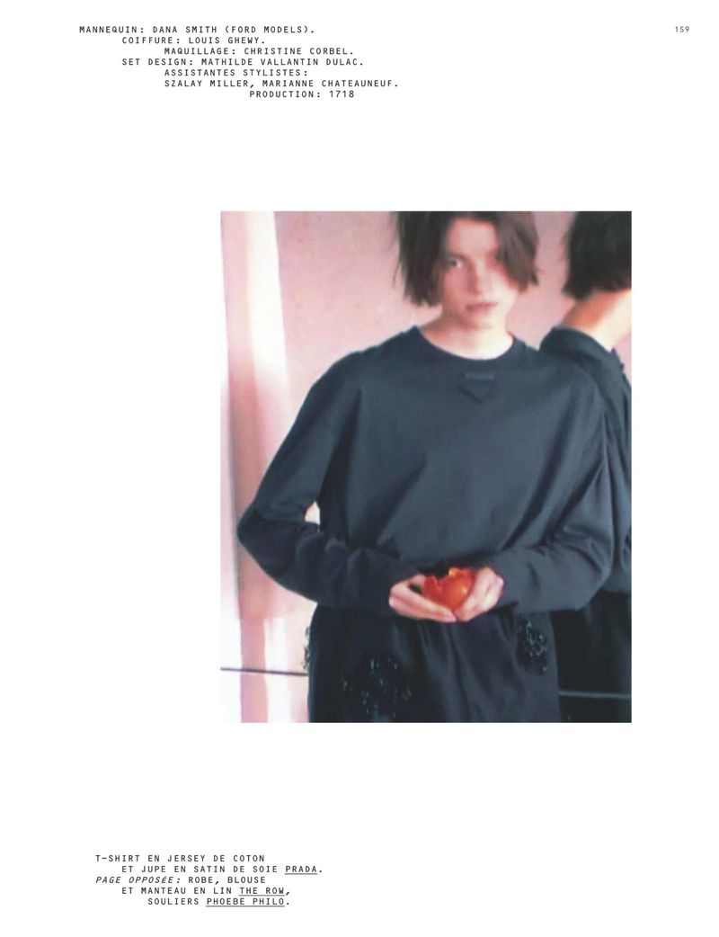 Fashion portrait of a young woman with short brown hair in a dark blue long-sleeved shirt, holding a red object in front of a pink background.