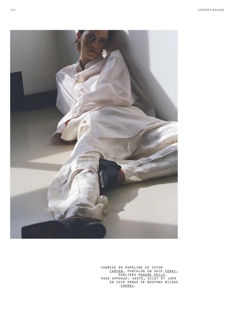 Fashion editorial image featuring a model reclining in a relaxed pose, wearing a white cotton shirt and silk pants, with visible black shoes.