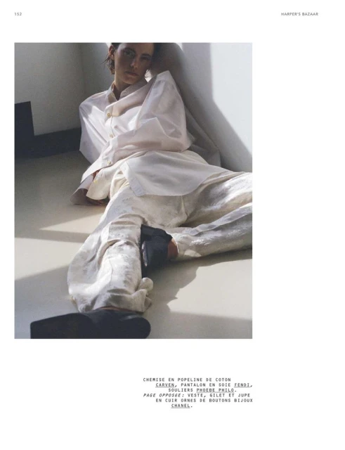 Fashion editorial image featuring a model reclining in a relaxed pose, wearing a white cotton shirt and silk pants, with visible black shoes.