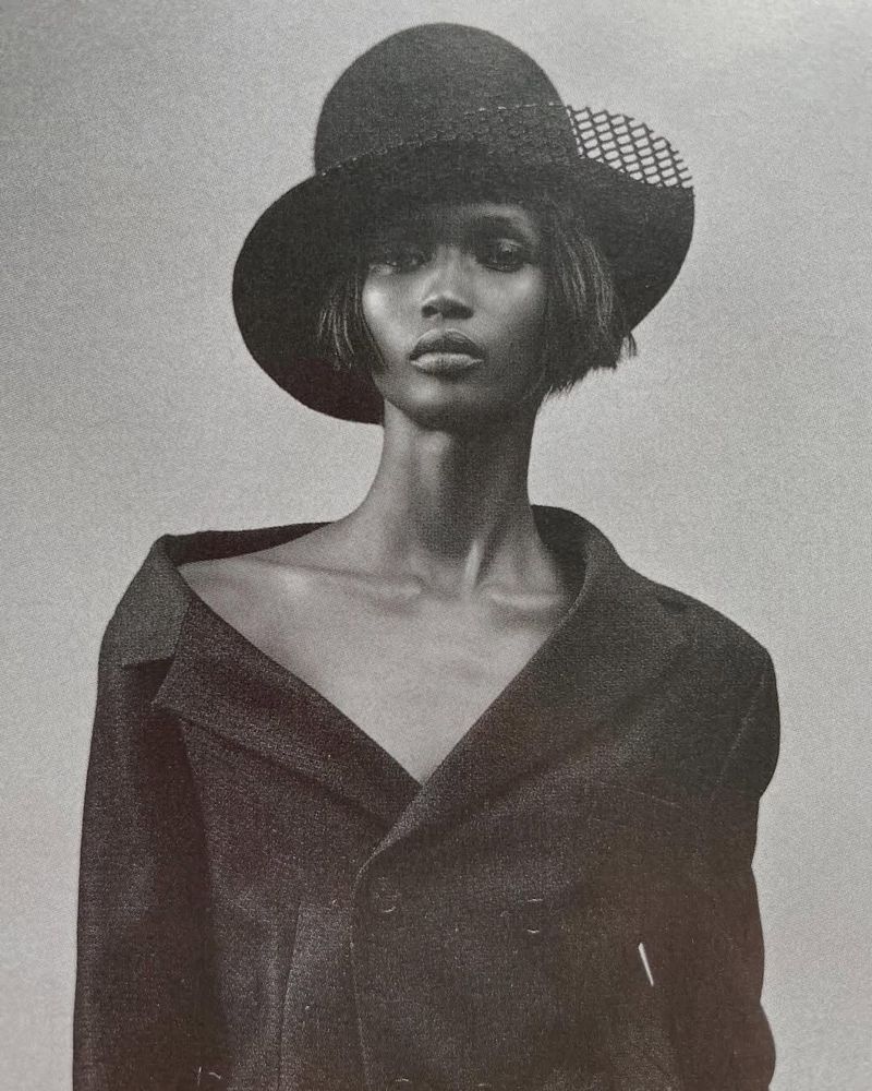 Model Jimai Hoth Gor wearing a dark hat and structured jacket in a black and white editorial portrait for Elle UK.