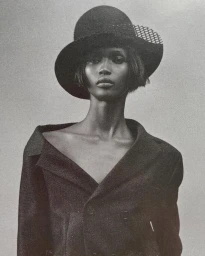 Model Jimai Hoth Gor wearing a dark hat and structured jacket in a black and white editorial portrait for Elle UK.