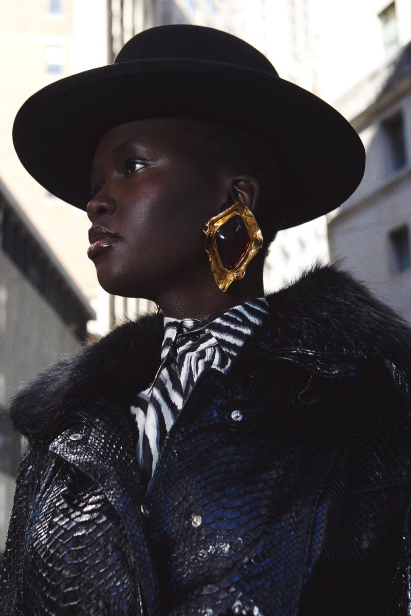 Portrait of a stylish Black woman wearing a black hat and a snakeskin-patterned jacket with fur collar in an urban environment.