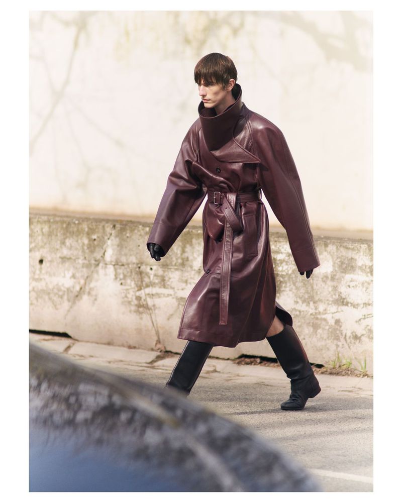 Male model in a long burgundy leather coat and tall black boots walking outdoors for SSAW Magazine