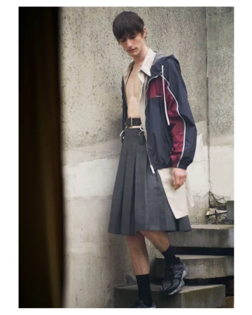 Model standing on concrete steps wearing a pleated skirt, unbuttoned shirt, and colour-blocked jacket for SSAW Magazine.