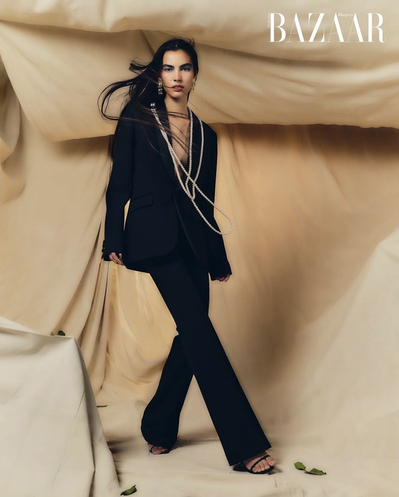 Model in black suit and long pearl necklace posing against draped fabric background for Harper's Bazaar Thailand