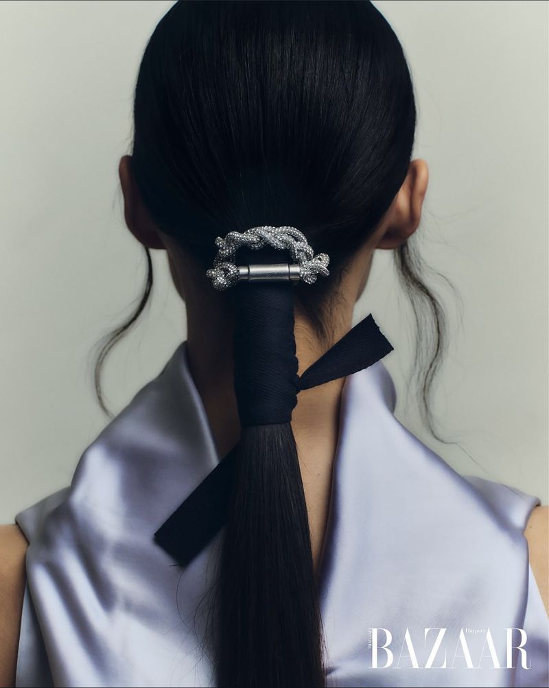 View of woman's dark hair styled in low ponytail with black ribbon and decorative metal hair clip against a soft cream backdrop.