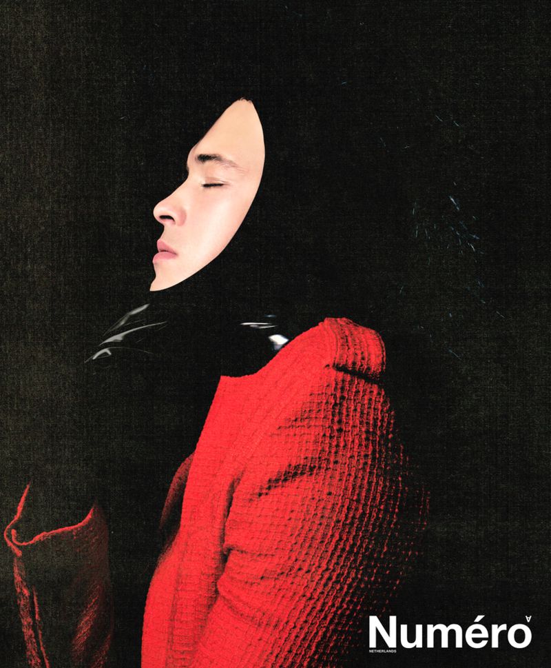 Fashion magazine portrait of an adult male with closed eyes wearing a red coat and black hood with black background.