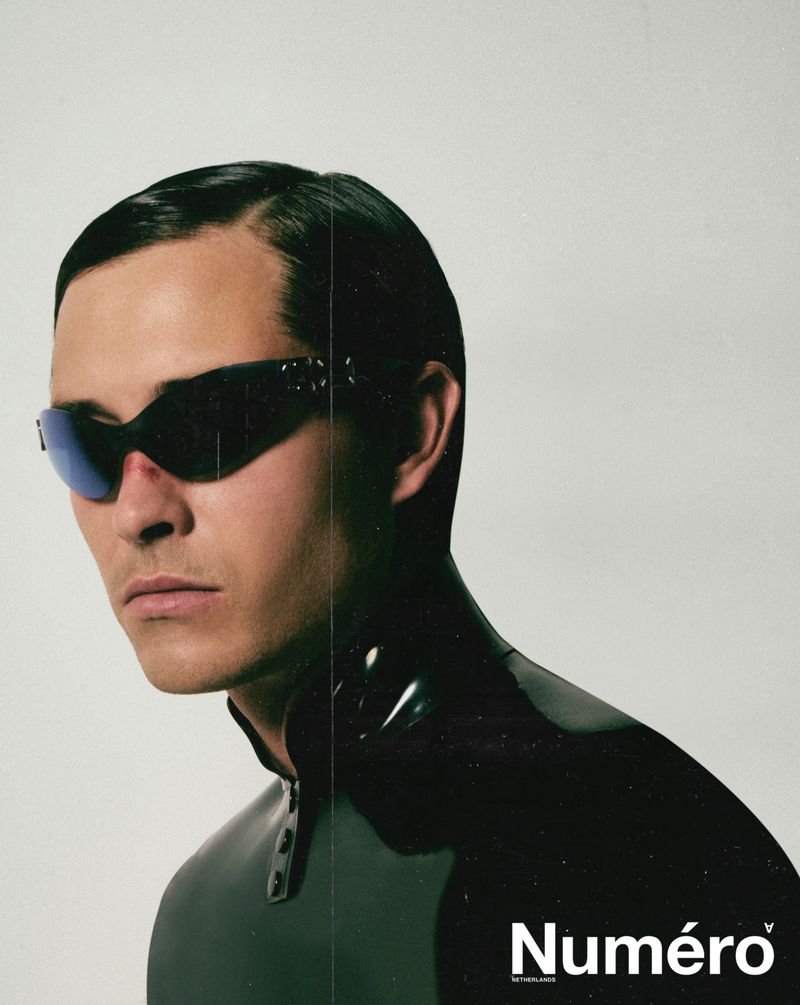 Close-up portrait of Francisco Lachowski wearing dark futuristic sunglasses and a black high-collar garment against a plain light background