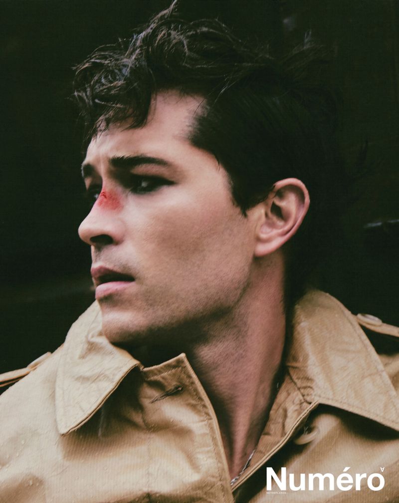 Portrait of a brunette male fashion model wearing a tan jacket with an injured makeup effect and the 'Numero' magazine logo at the bottom.