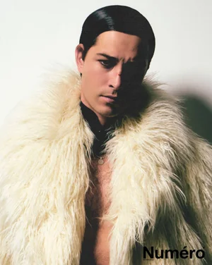 Francisco Lachowski wearing a cream faux fur coat against a plain white background for a fashion editorial portrait