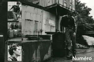 Francisco Lachowski in a black jacket and jeans leaning against a metal drum in an industrial alley for Numéro Homme Netherlands