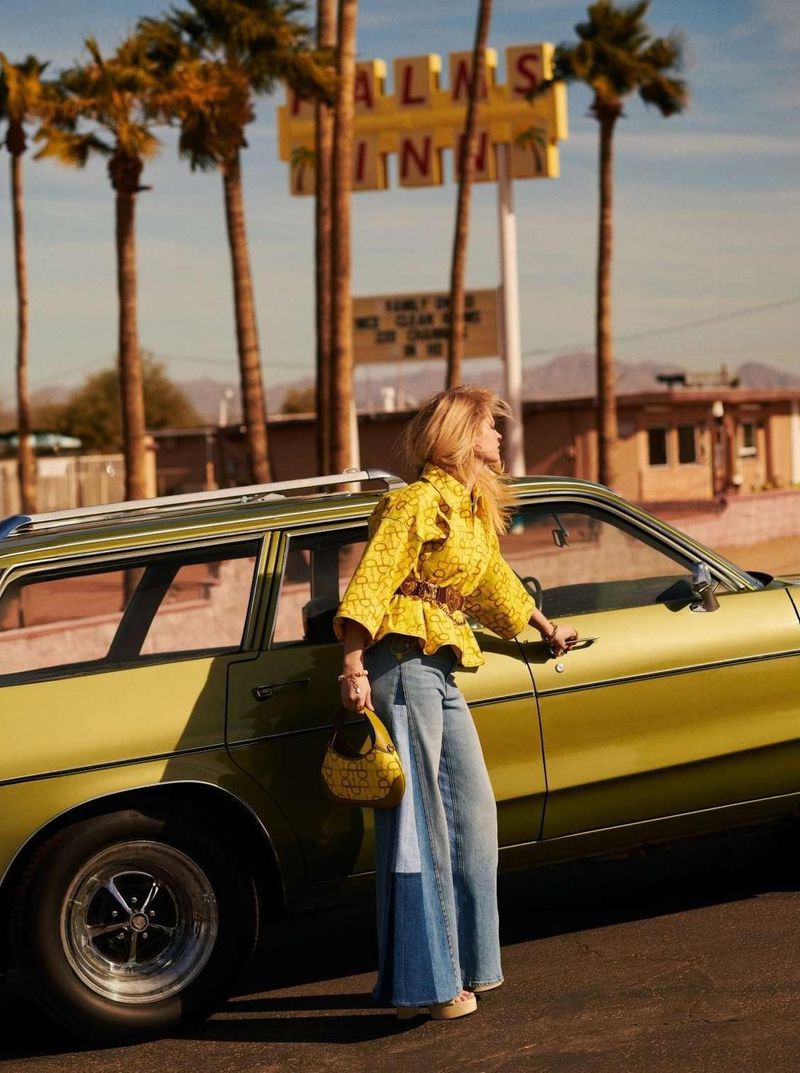 Adult woman in yellow patterned top and wide-leg jeans standing by a green station wagon in front of a Palm Springs hotel.
