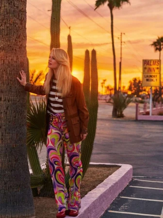 Woman poses in retro patterned pants and jacket by palm tree at sunset near a Palms Inn motel in Palm Springs, California.