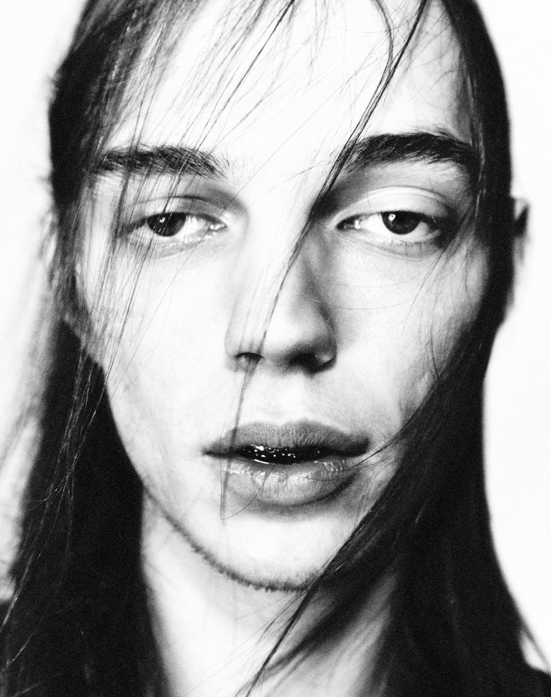 Monochrome portrait of a young adult with dark hair falling across their face, a stark white background and shallow depth of field.